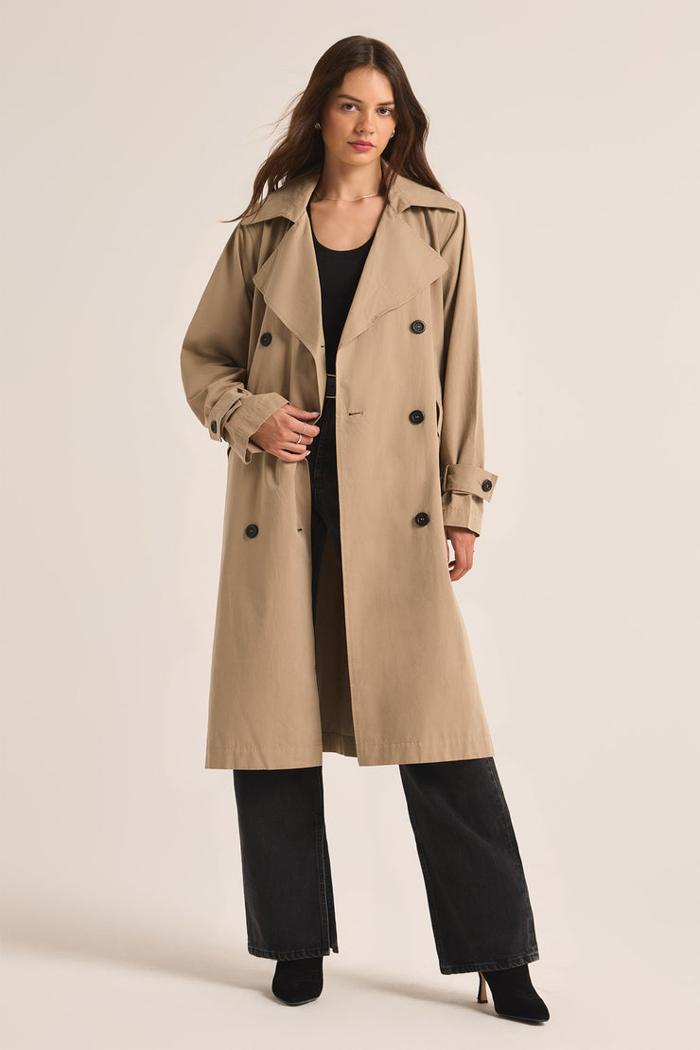 Woman wearing a beige trench coat on a plain background