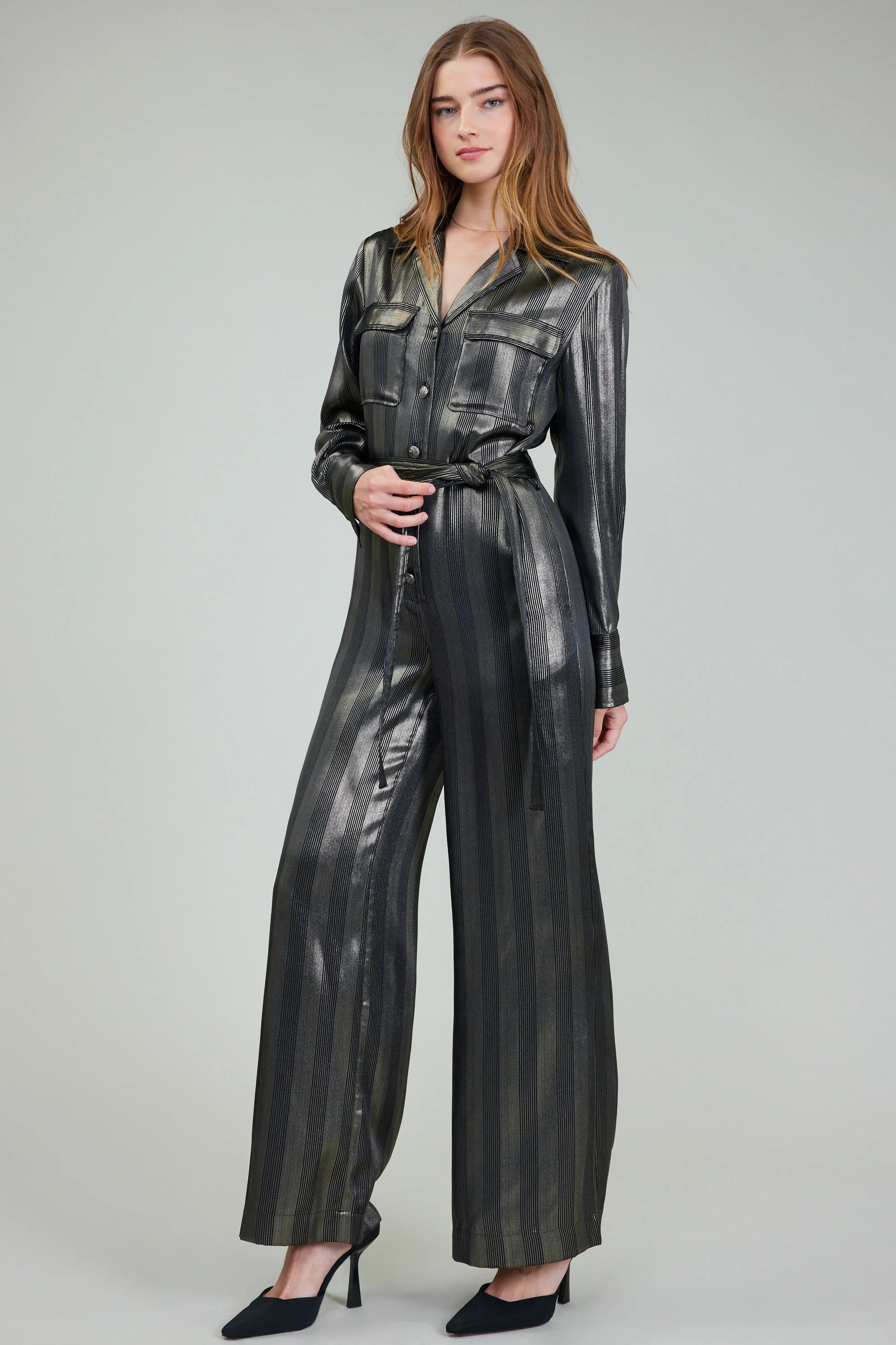 Woman wearing a shiny black jumpsuit on a plain background