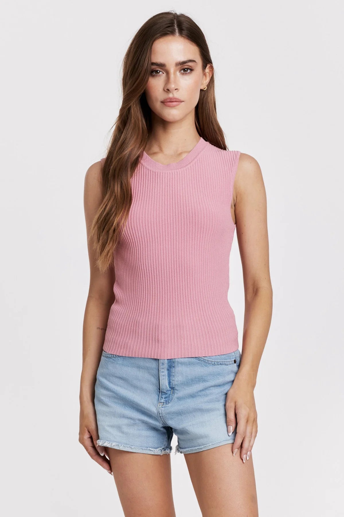 Woman wearing a pink sleeveless top and denim shorts on a white background
