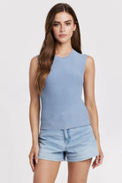 Woman wearing a light blue sleeveless top and denim shorts on a white background