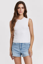 Woman wearing a white sleeveless top and denim shorts on a plain background