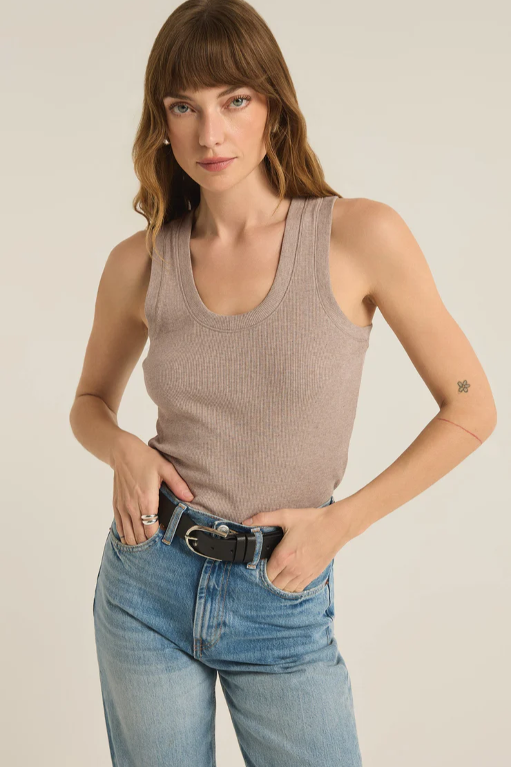 Woman wearing a beige tank top and blue jeans against a plain background