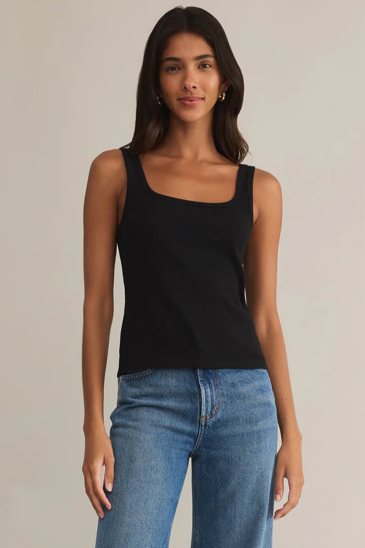 Woman wearing a black tank top and blue jeans against a neutral background