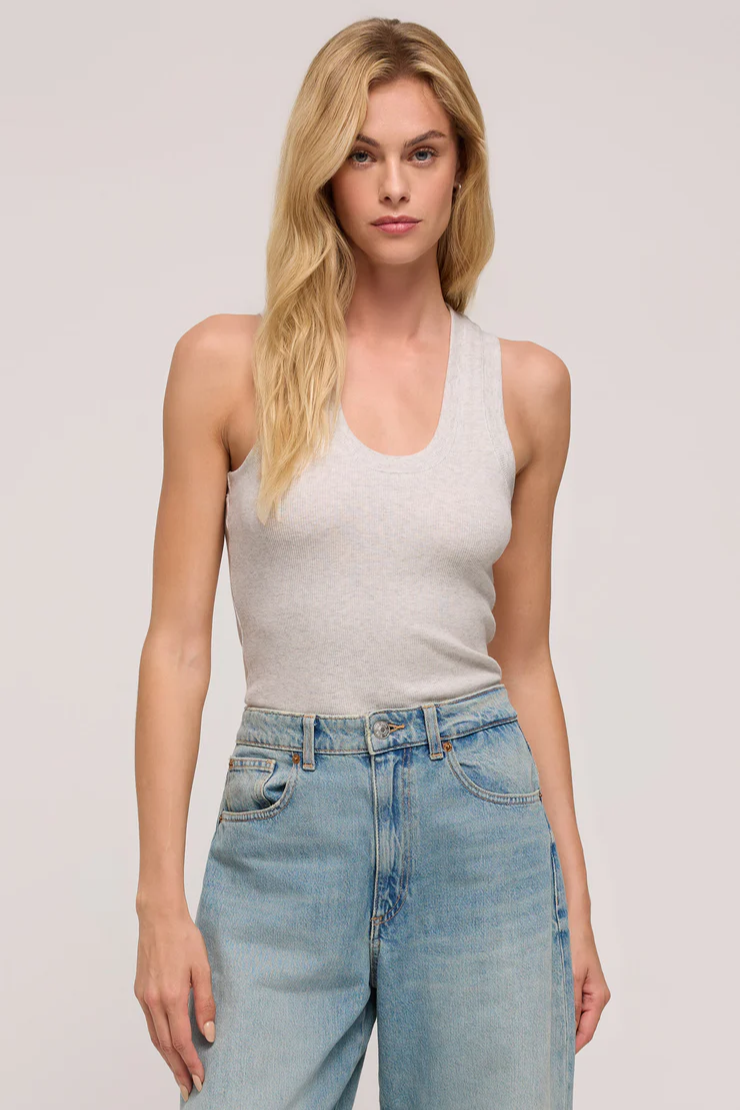 Woman wearing a gray tank top and blue jeans against a plain background