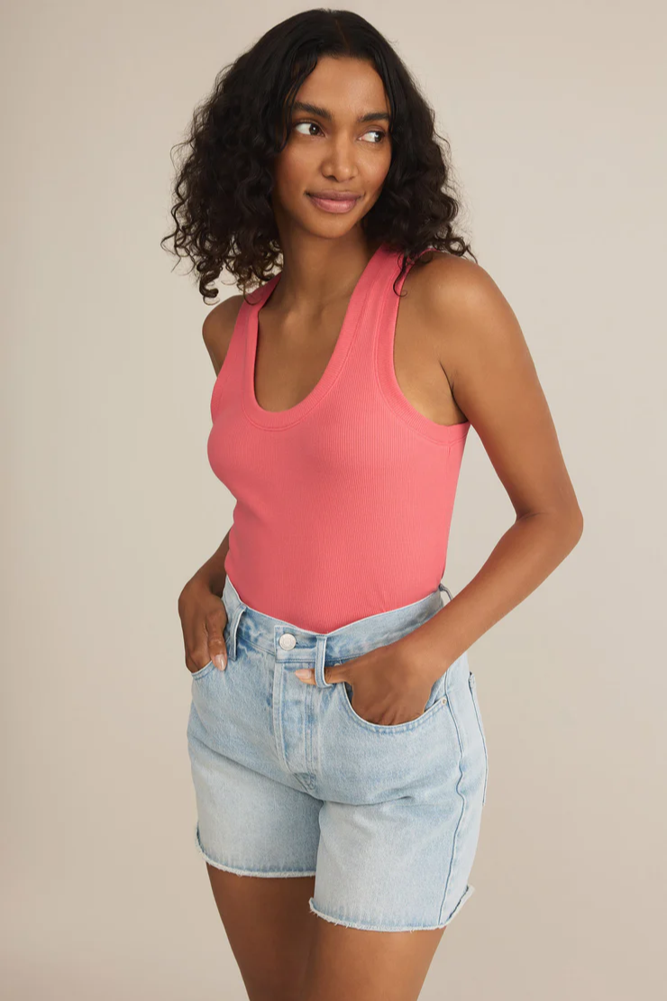 Woman wearing a pink tank top and denim shorts against a beige background