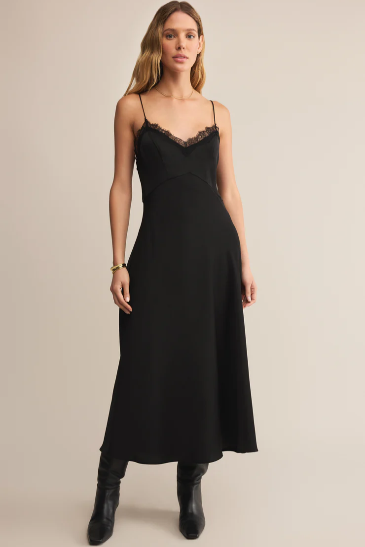 Woman wearing a black slip dress with lace details on a beige background