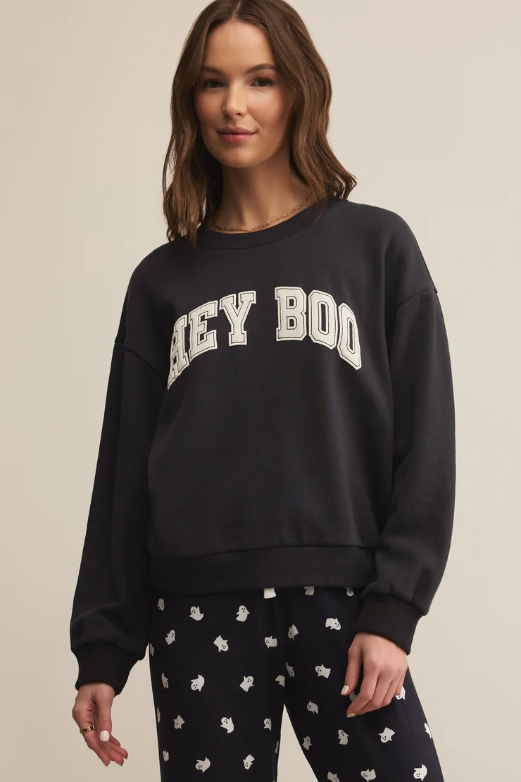 Woman wearing a black sweatshirt with 'HEYY BOY' text and patterned pants on a beige background