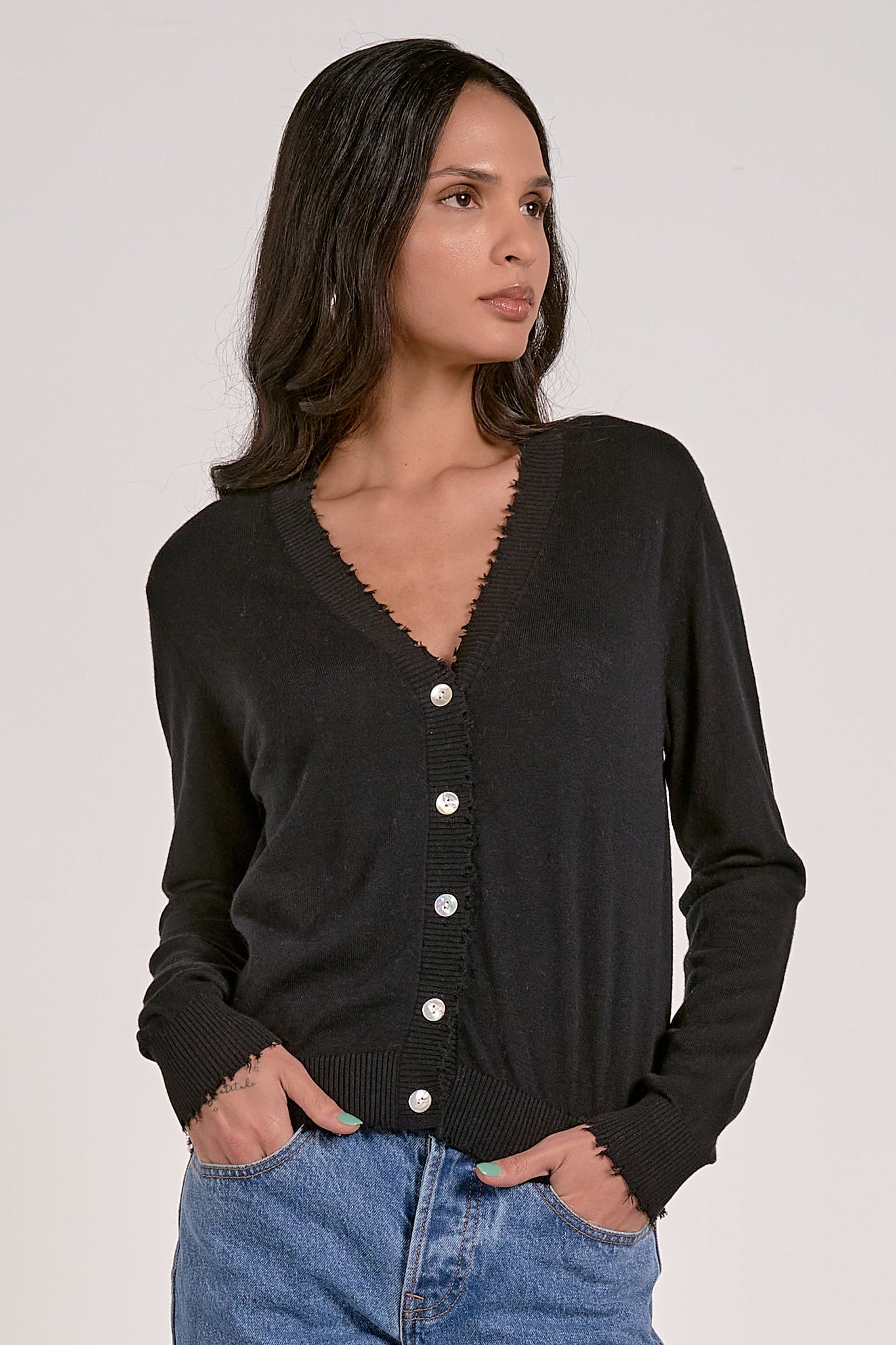 Woman wearing a black cardigan with white buttons on a plain background