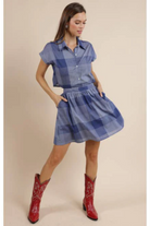 Woman wearing a blue plaid dress with red cowboy boots on a beige background