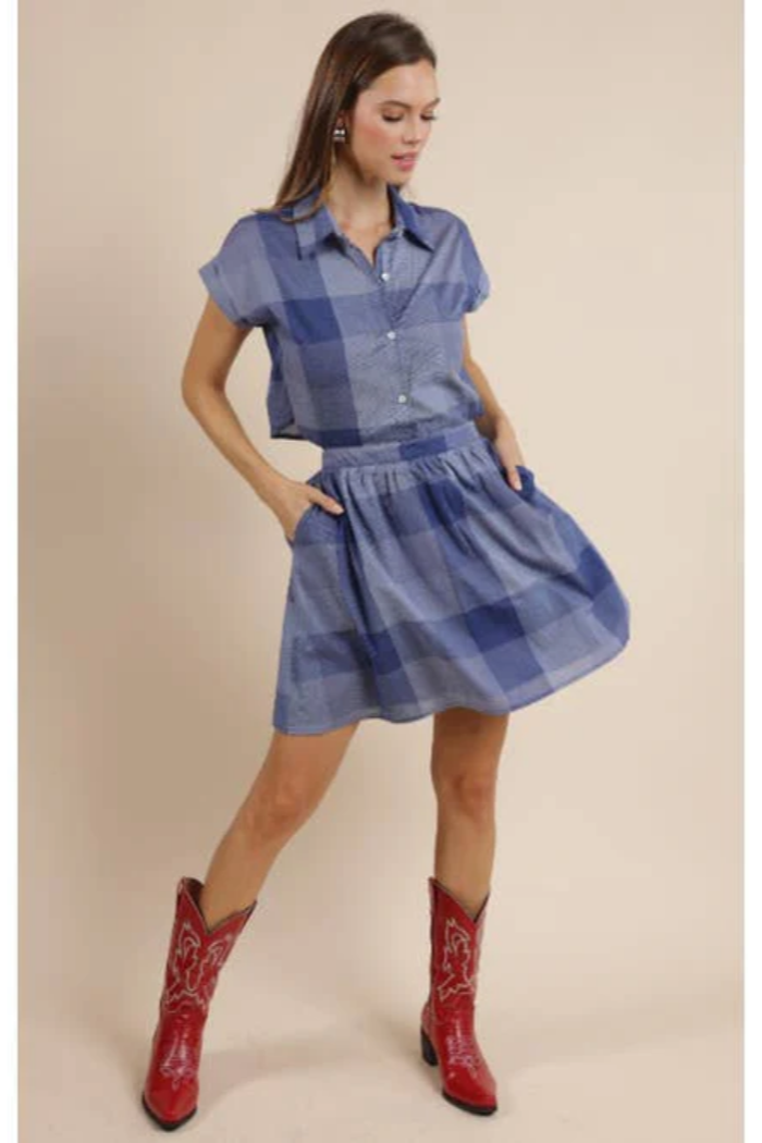 Woman wearing a blue plaid dress with red cowboy boots on a beige background