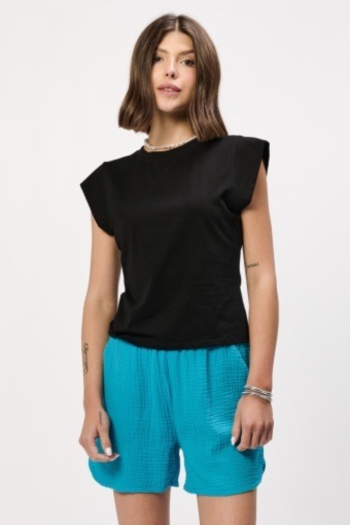 Woman wearing a black sleeveless top and turquoise shorts on a white background