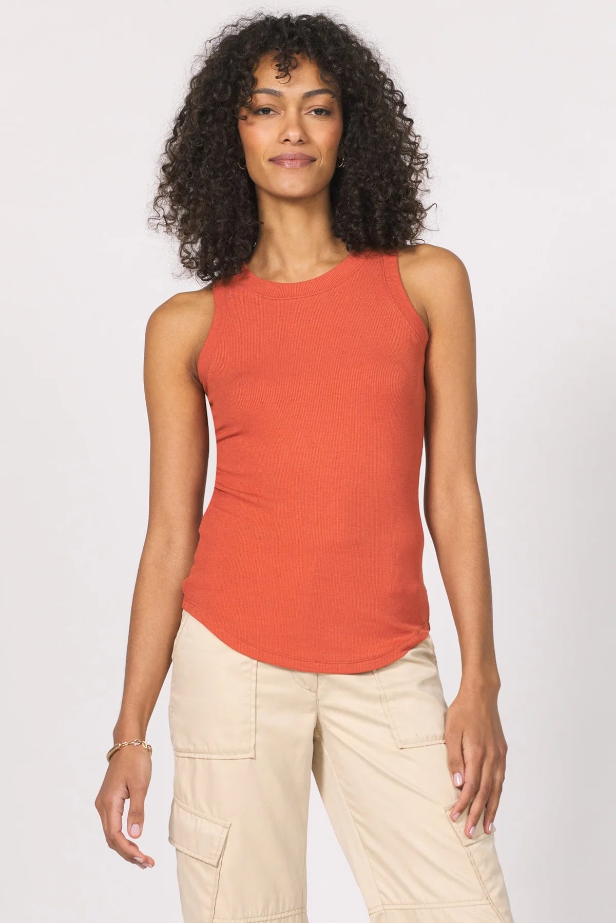 Woman wearing an orange sleeveless top and beige pants against a white background