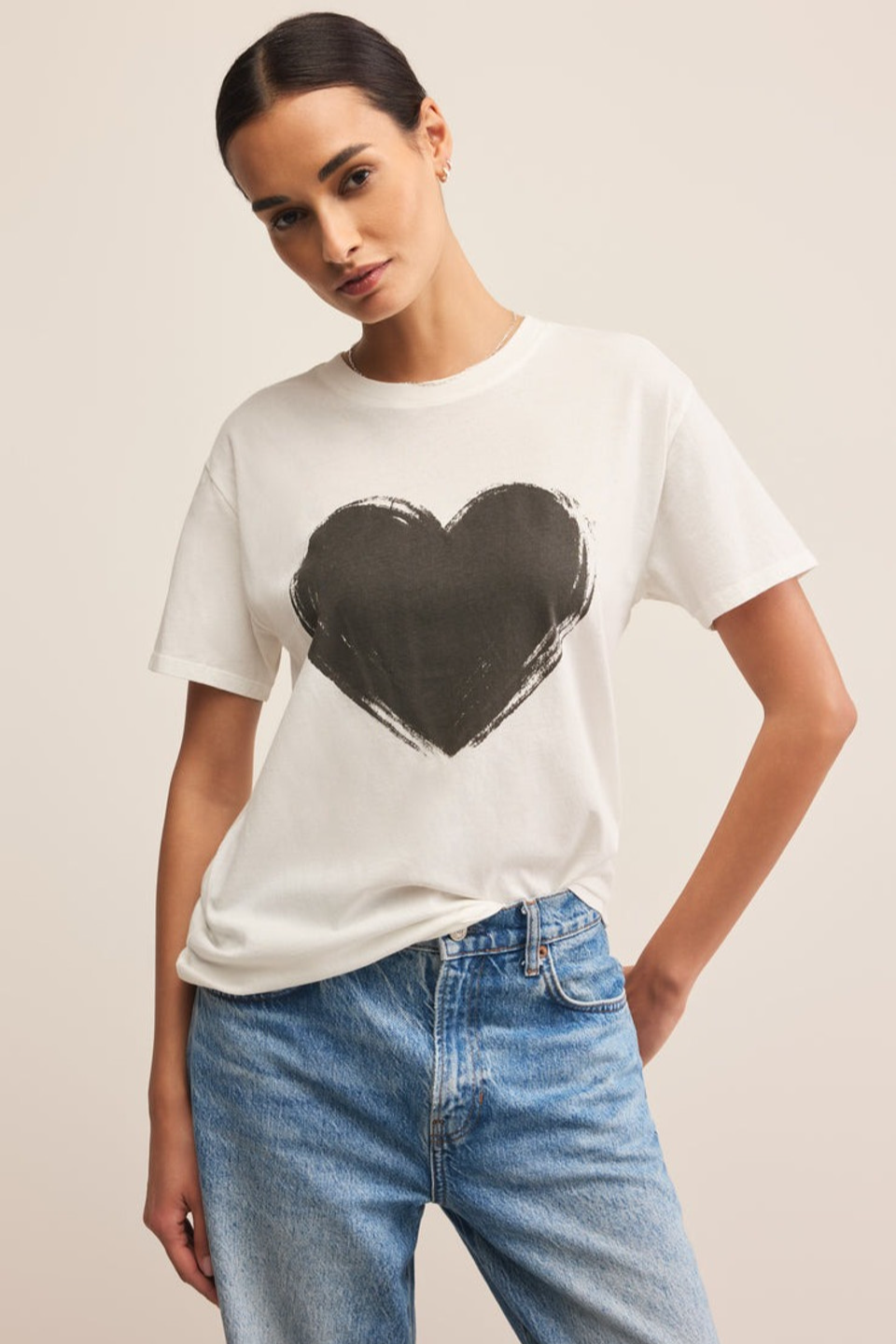 Woman wearing a white t-shirt with a black heart design and blue jeans on a beige background