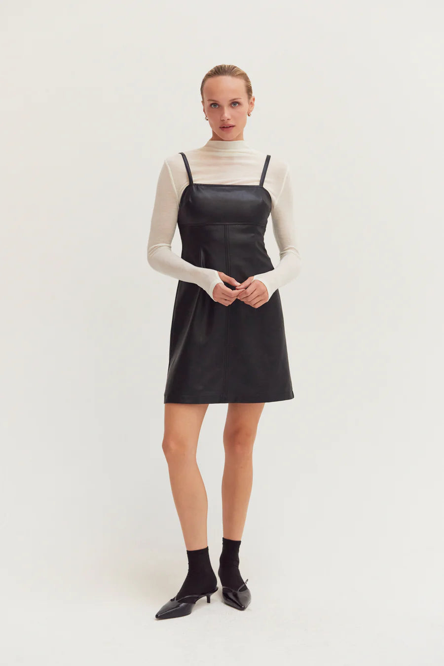 Woman wearing a black dress over a white long-sleeve shirt on a white background