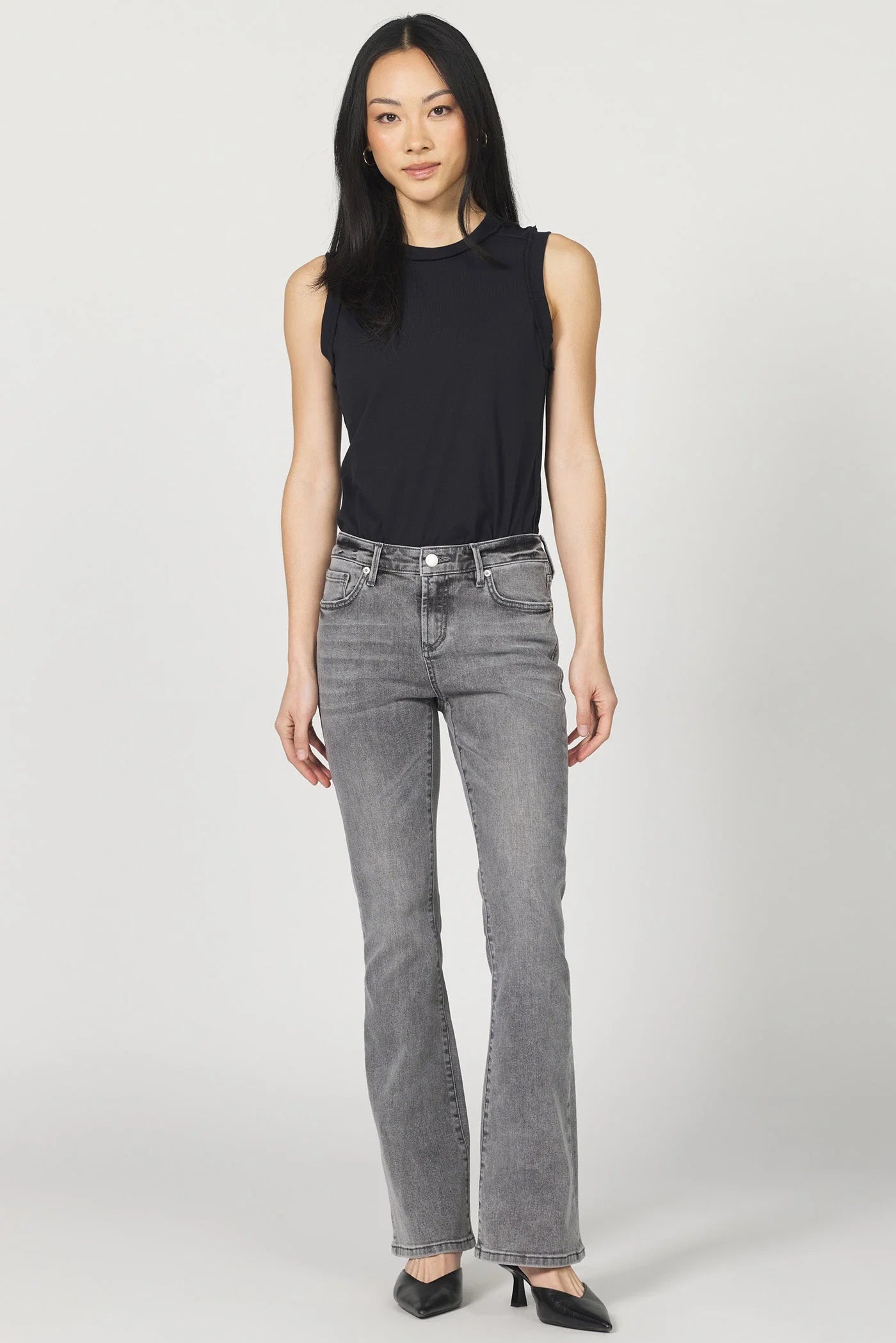 Woman wearing a black sleeveless top and gray jeans on a white background