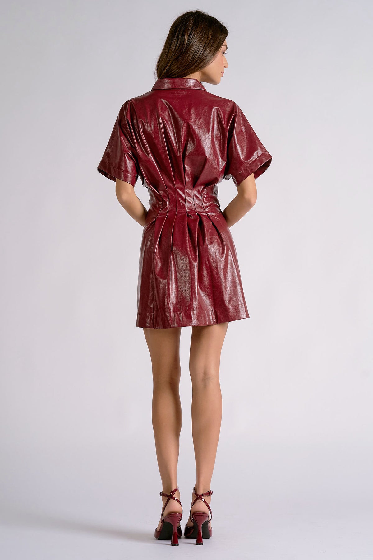 Back view of oxblood faux leather mini dress with pleated waist detail