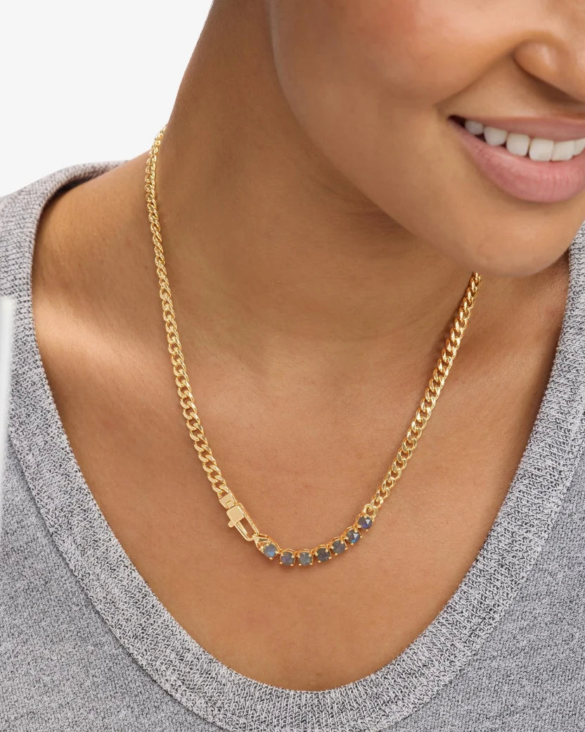 Woman wearing gold curb chain necklace with blue-gray labradorite stones over gray sweater