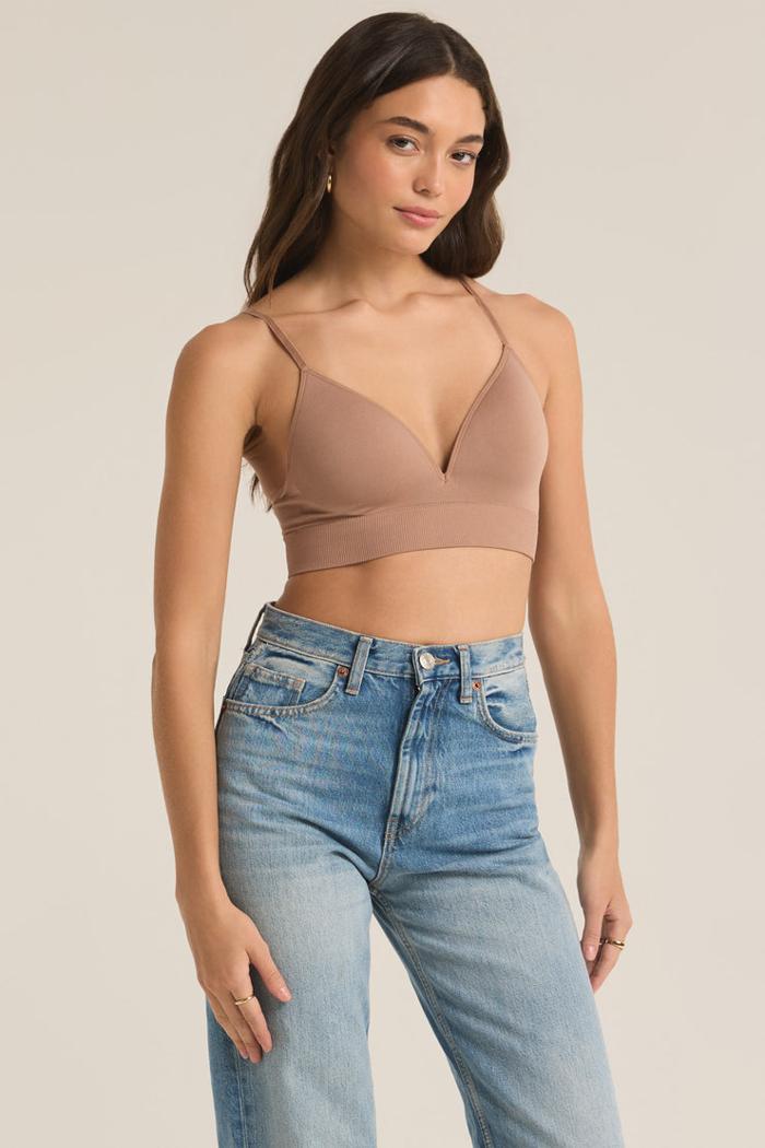 Woman wearing a beige crop top and blue jeans on a plain background