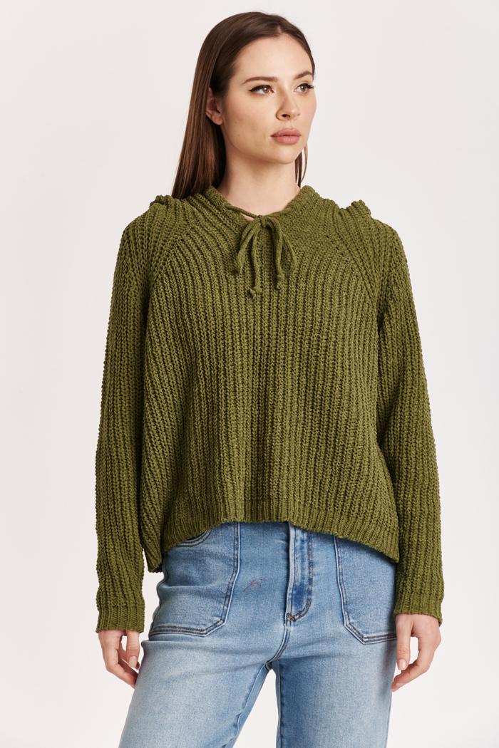 Woman wearing a green knitted sweater and blue jeans on a white background