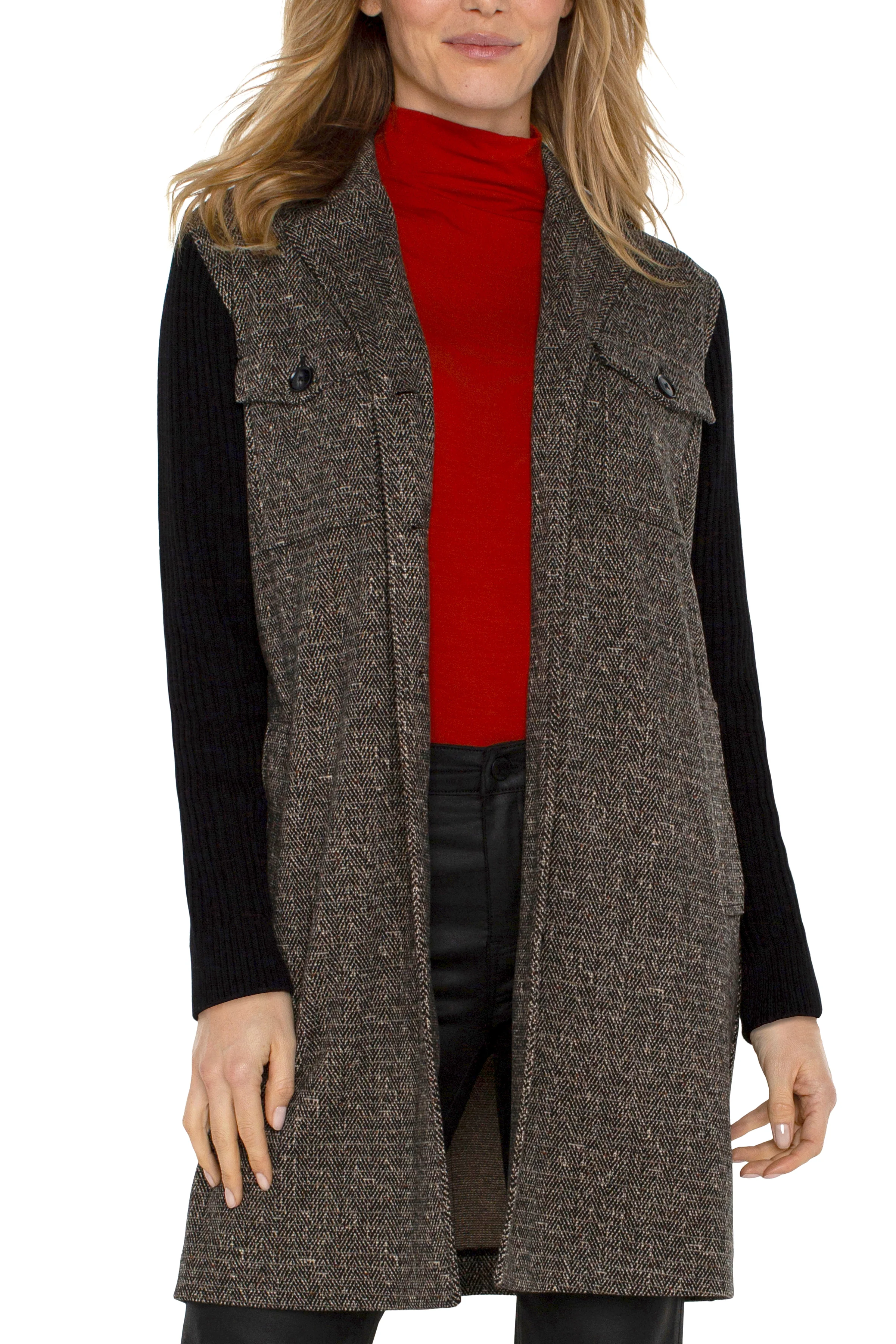 Woman wearing a brown tweed vest over a red turtleneck and black long-sleeve shirt on a white background