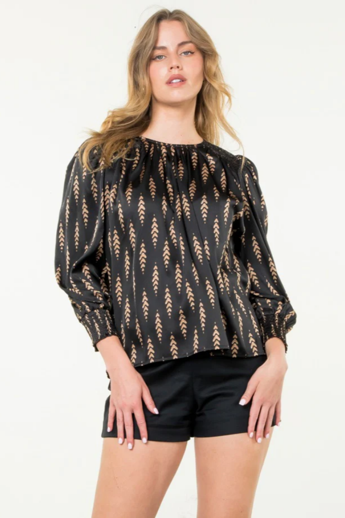 Woman wearing a black patterned blouse and black shorts on a white background