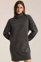 Woman wearing a dark gray turtleneck dress against a plain background