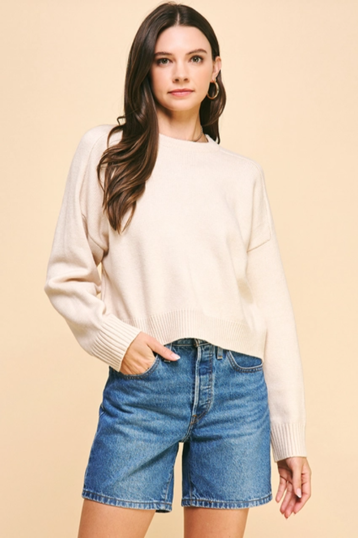 Woman wearing a cream sweater and denim shorts against a beige background