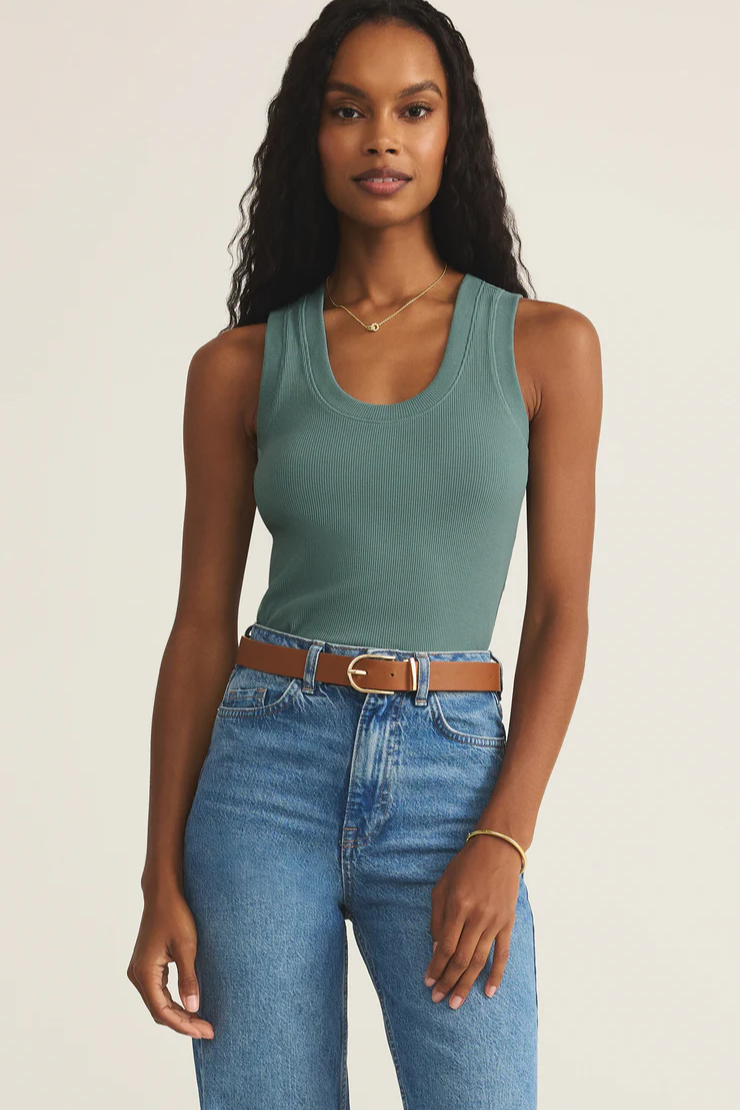 Woman wearing a teal tank top and blue jeans with a beige background