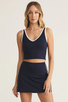 Woman wearing a navy blue tank top and skirt with white trim on a beige background