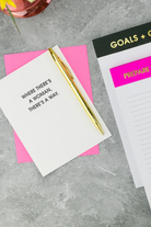 Notebook with a gold pen on pink paper, with motivational quote and 'Goals + Goals' planner in the background.