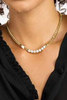 Gold chain necklace with small diamonds on a person wearing a black top.
