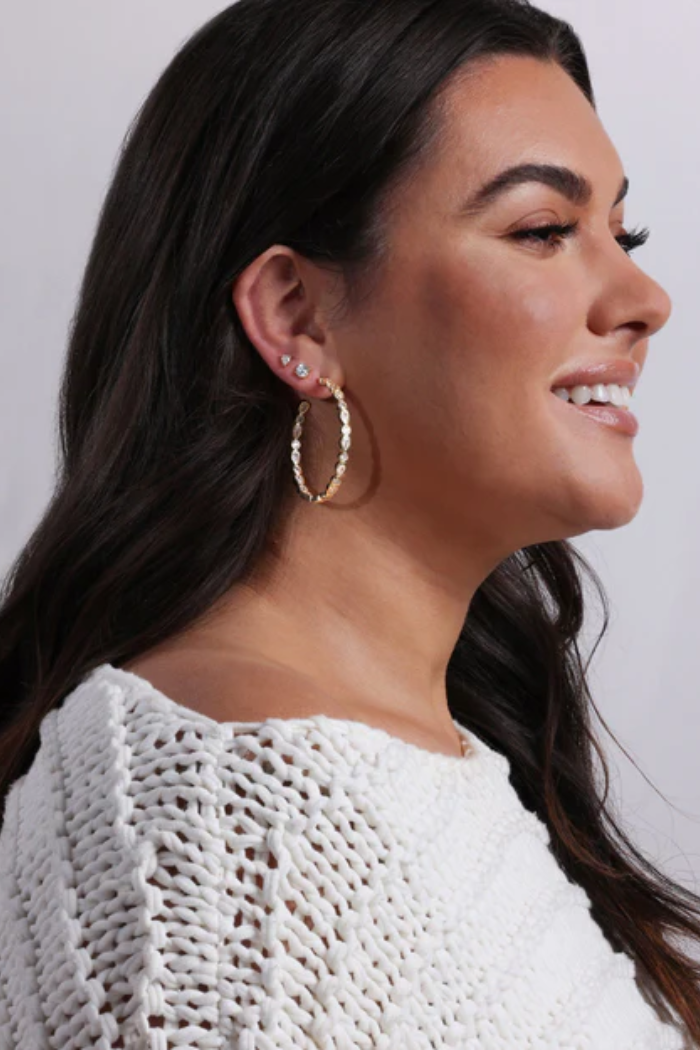 Woman wearing gold hoop earrings with a plain background
