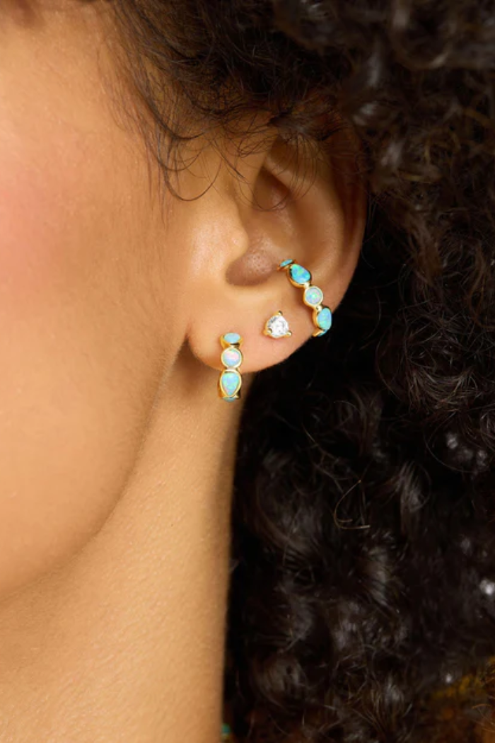 Close-up of a person wearing turquoise and gold hoop earrings with small gemstones.