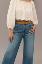 Person wearing a white blouse with eyelet details and blue jeans on a gray background