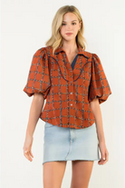Woman wearing a rust-colored checkered blouse with puffed sleeves on a white background