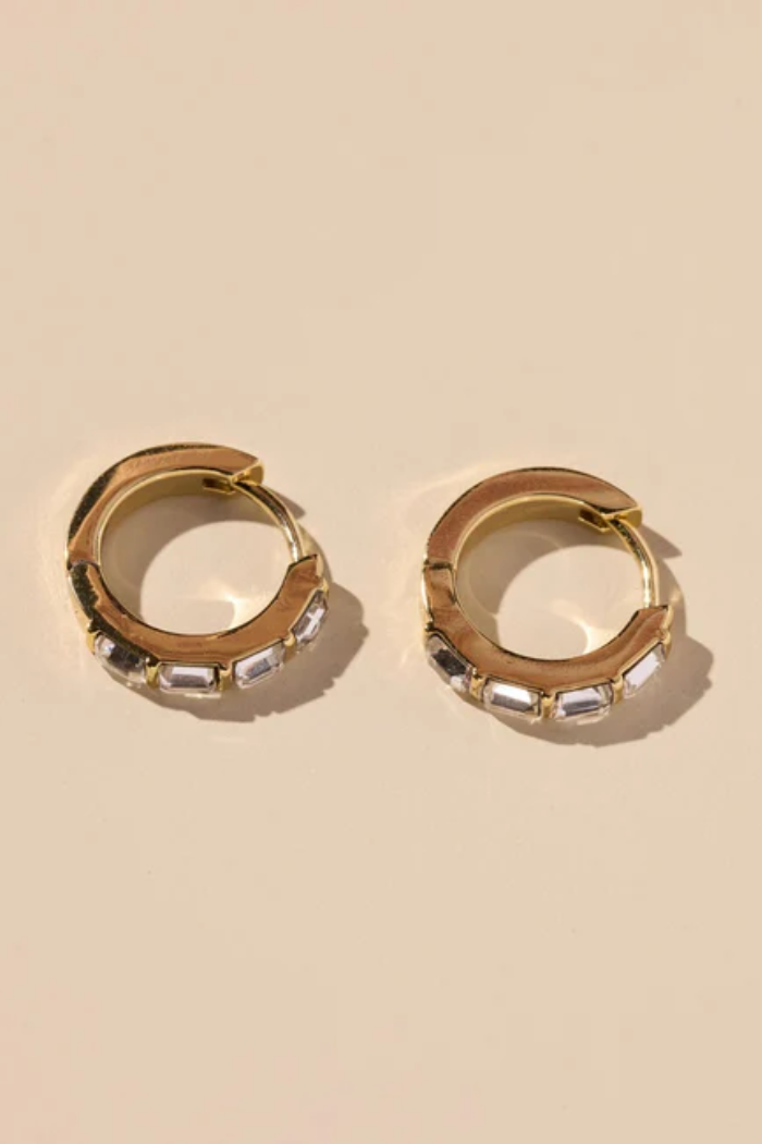 Gold hoop earrings with embedded stones on a beige background