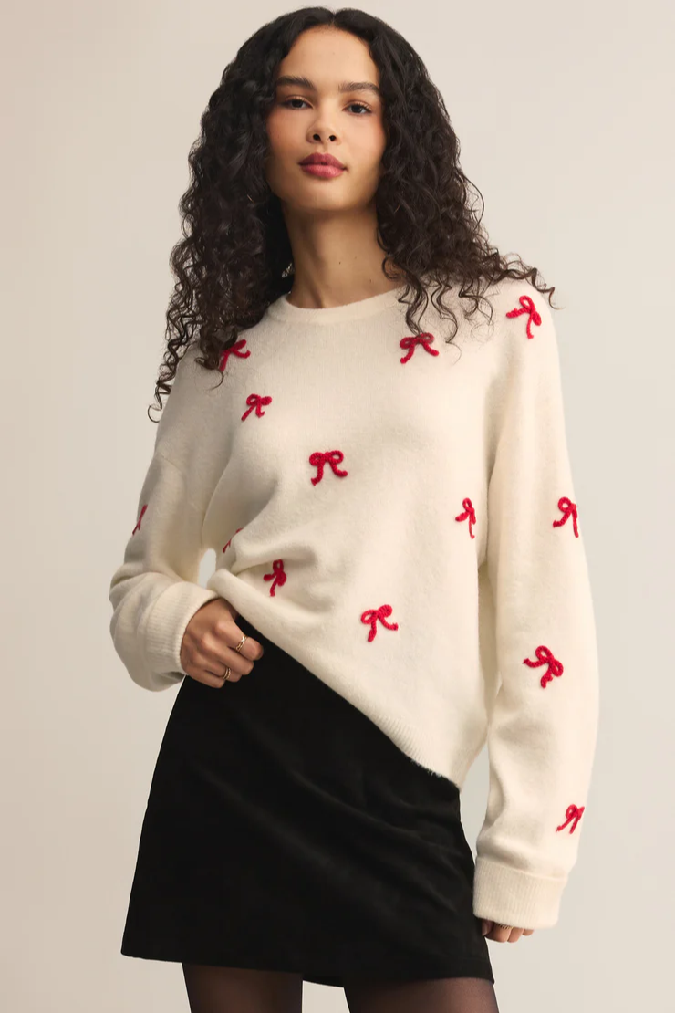 Woman wearing a cream sweater with red bow patterns on a plain background