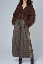 Person wearing a brown textured cardigan over a plaid dress with a white background