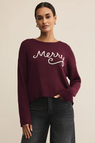 Woman wearing a burgundy sweater with 'Merry' text on a beige background