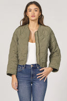 Woman wearing an olive green quilted jacket and blue jeans on a white background
