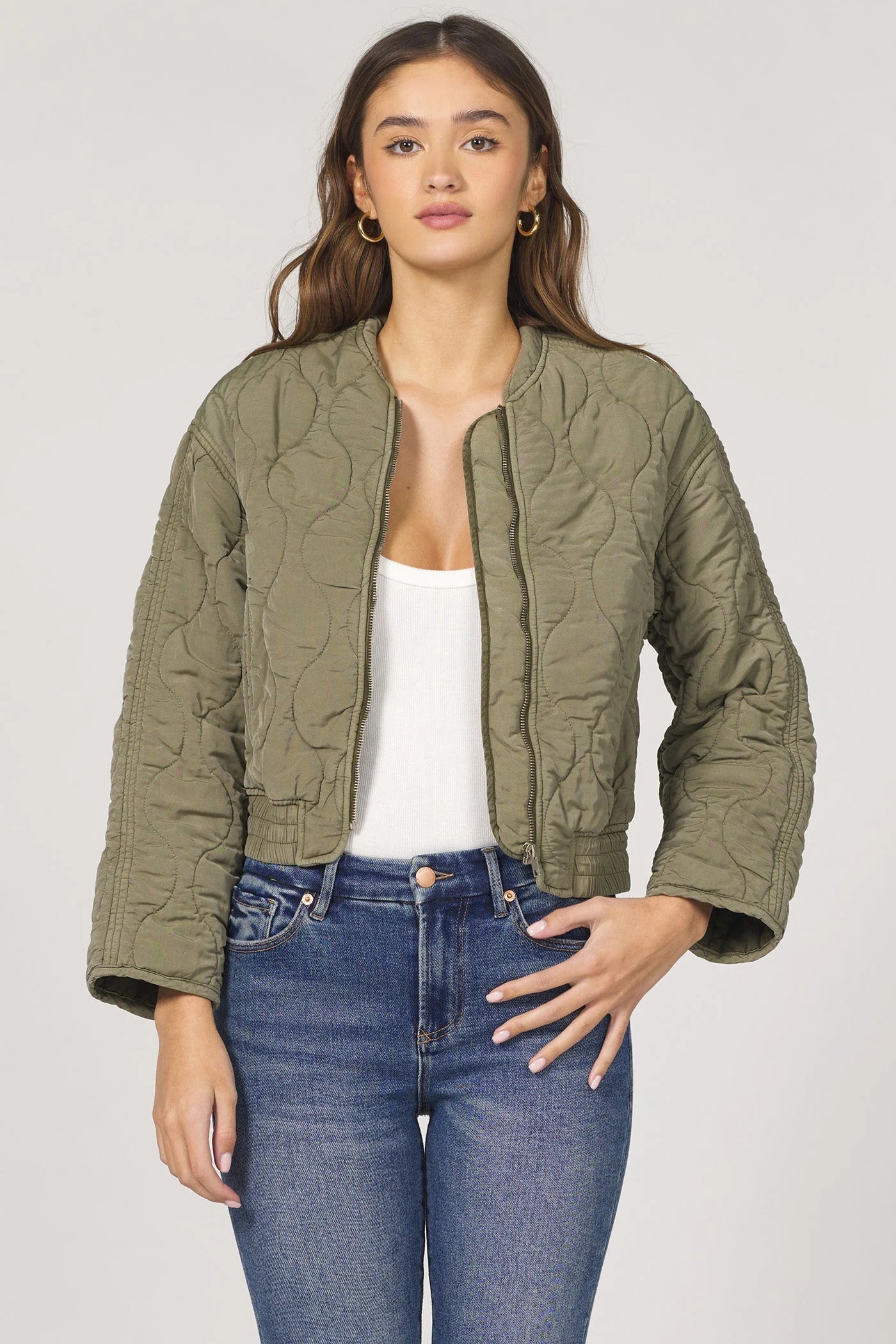 Woman wearing an olive green quilted jacket and blue jeans on a white background