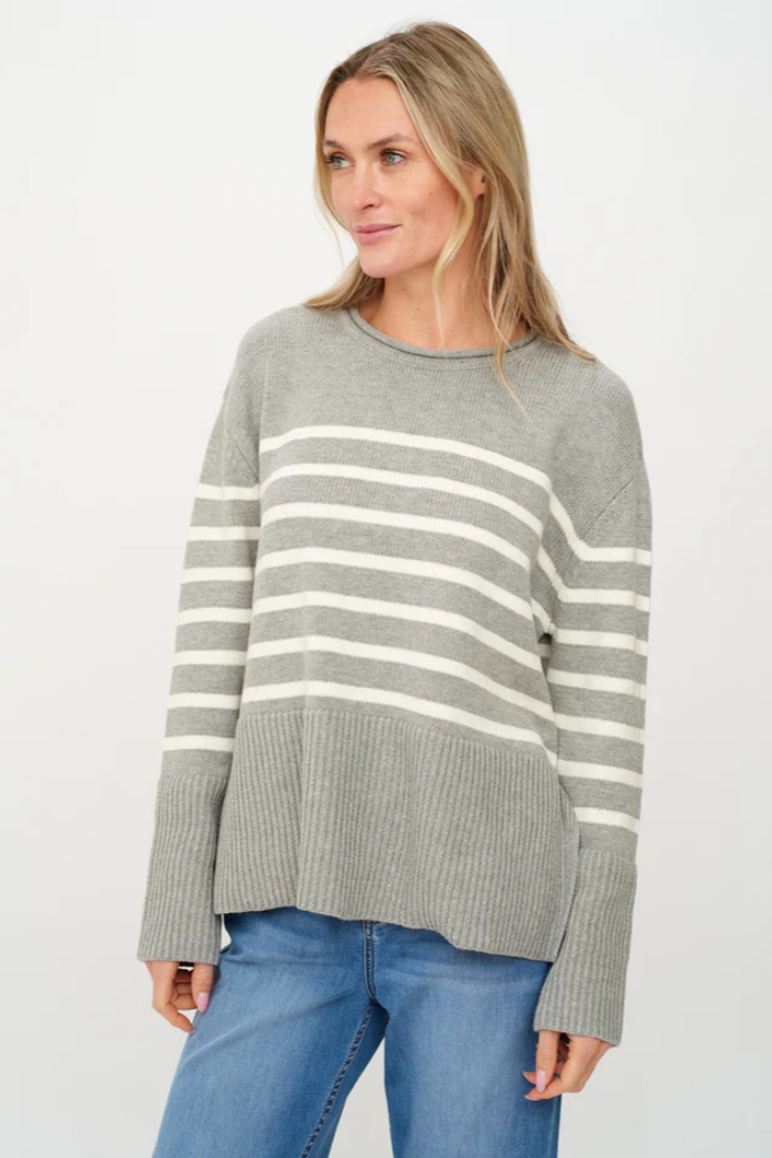 Woman wearing a gray sweater with white stripes and blue jeans on a white background