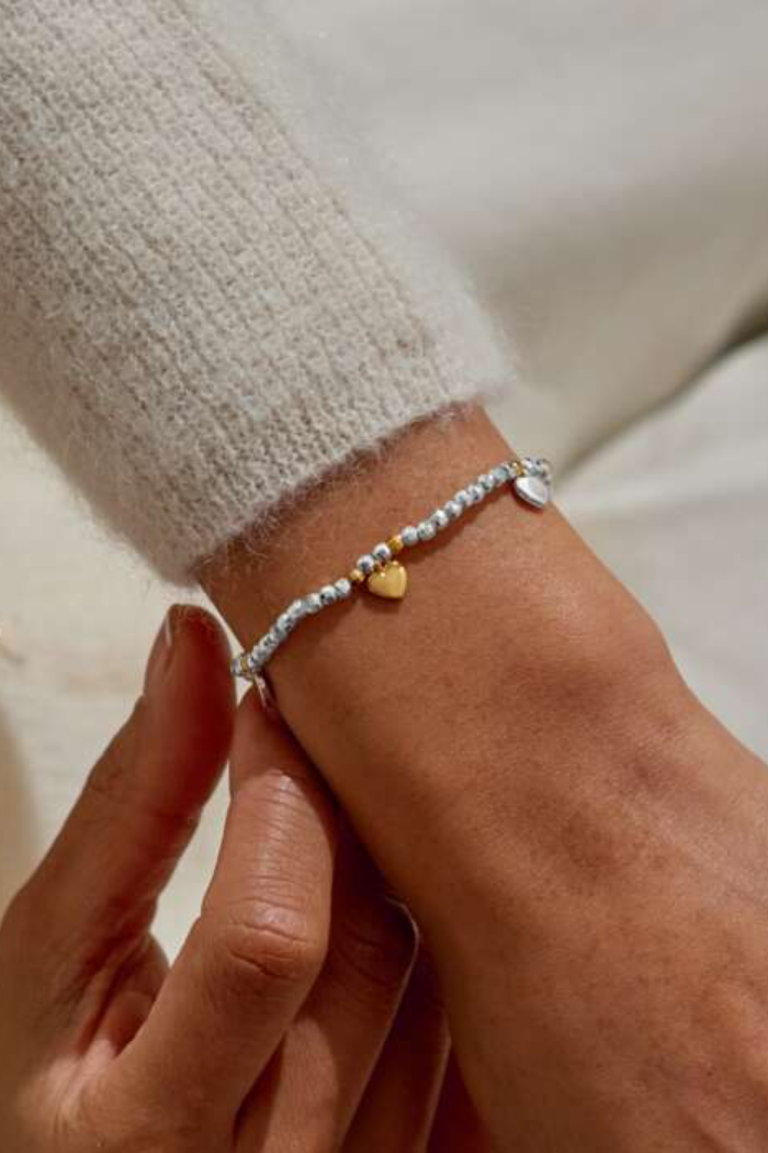Close-up of a wrist wearing a silver bracelet with a heart charm.