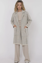 Woman wearing a patterned coat and beige pants on a white background