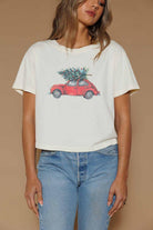 Person wearing a white t-shirt with a graphic of a red car carrying a Christmas tree on a beige background
