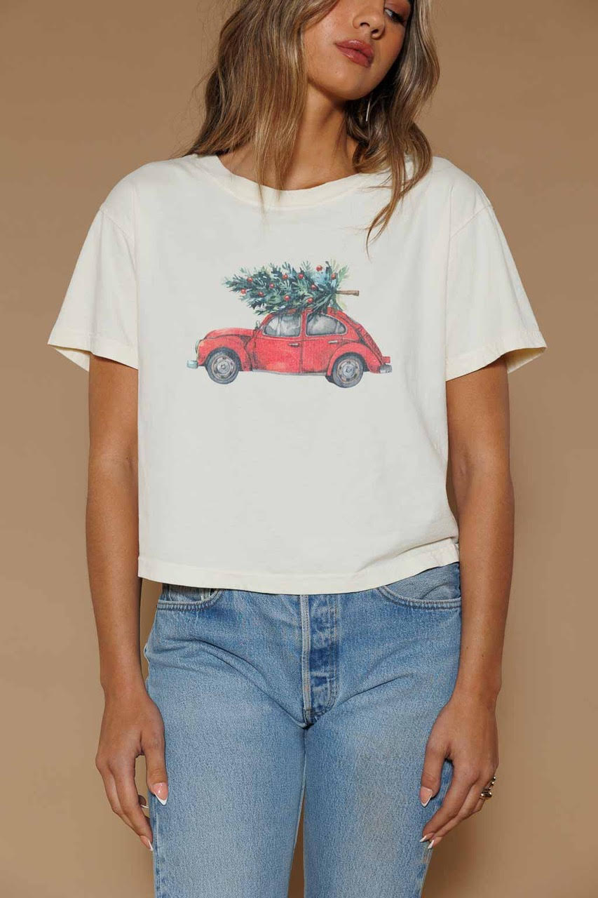 Person wearing a white t-shirt with a graphic of a red car carrying a Christmas tree on a beige background