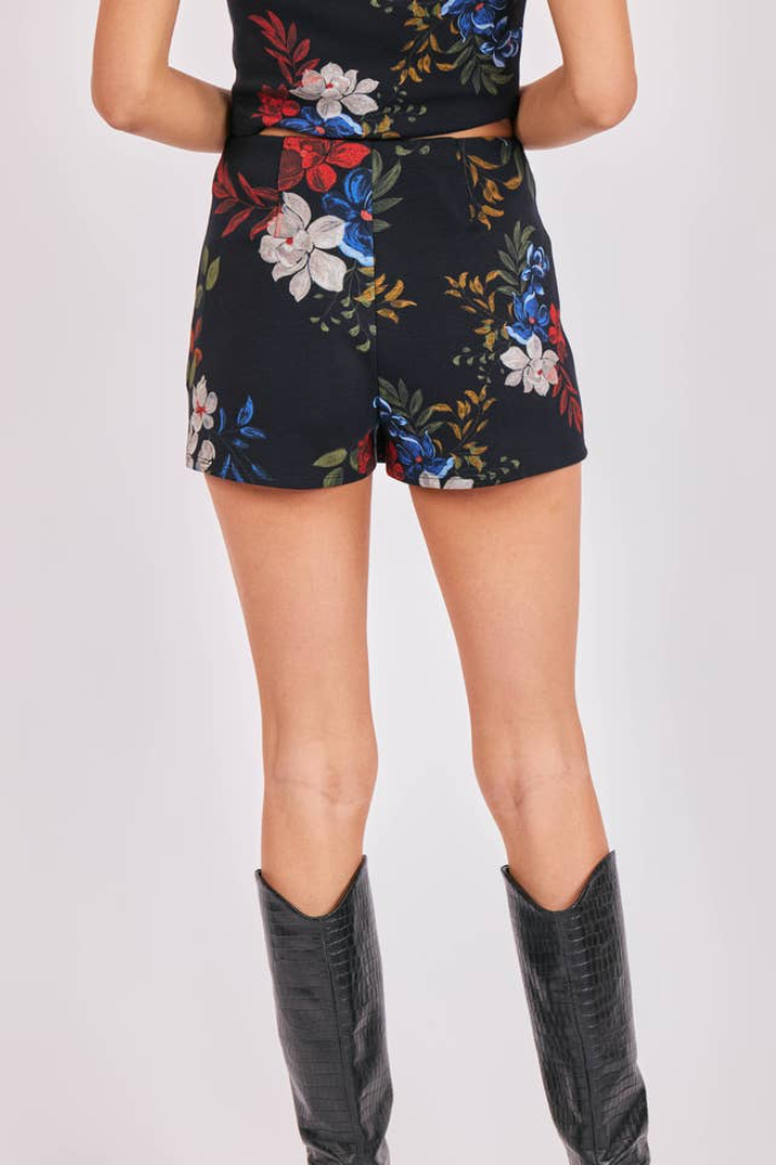 Person wearing a black floral skirt with black knee-high boots on a white background