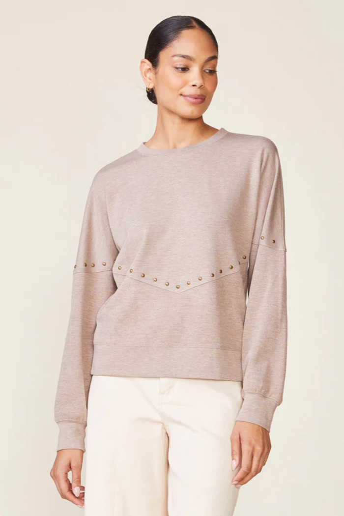 Woman wearing a beige sweater with pearl embellishments on a plain background