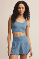 Woman wearing a blue ribbed crop top and shorts on a beige background