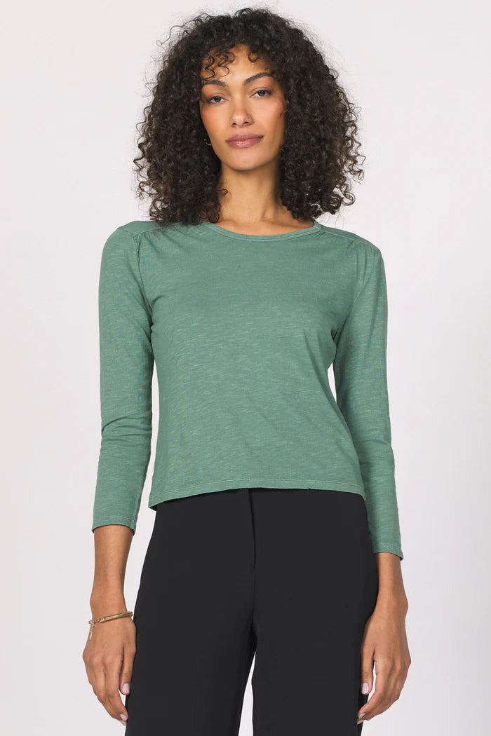 Woman wearing a green long-sleeve top and black pants against a white background